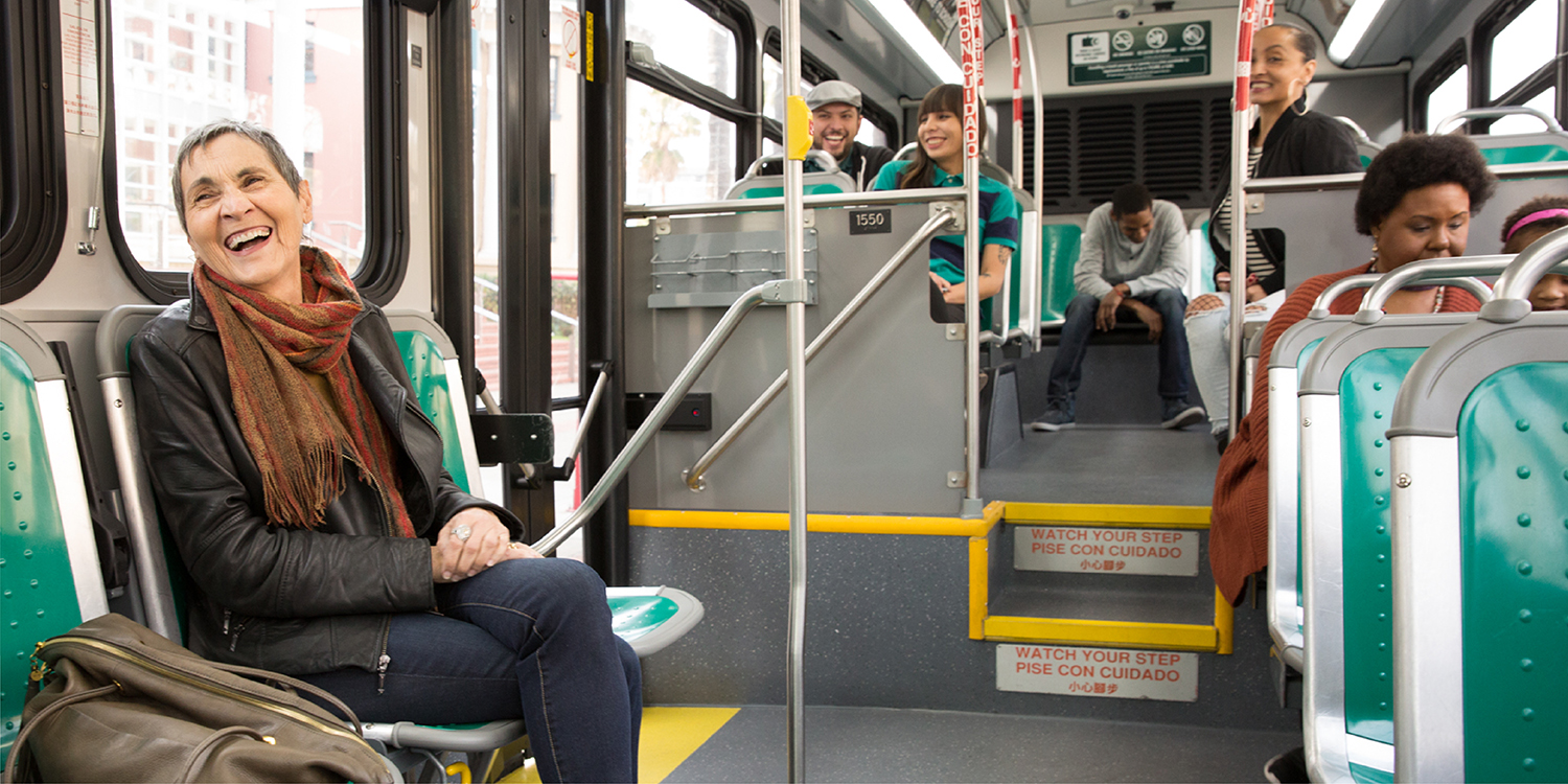 Woman sitting on bus, smiling at someone off camera