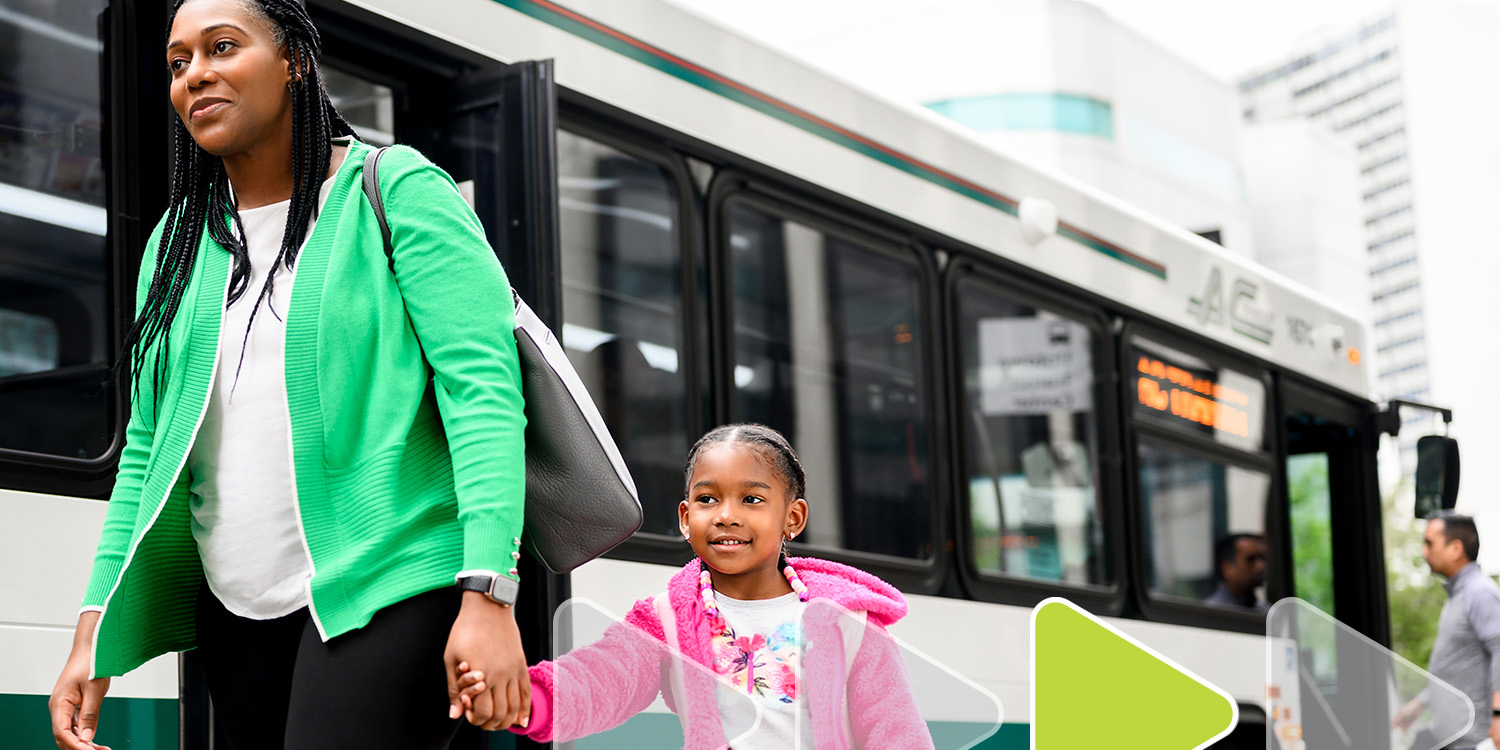Woman walking with her daughter, along the side of a bus