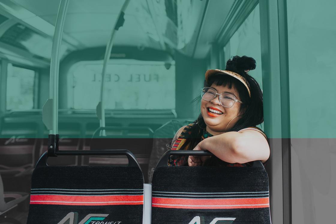 Women in a visor and glasses smiling, while sitting on bus.
