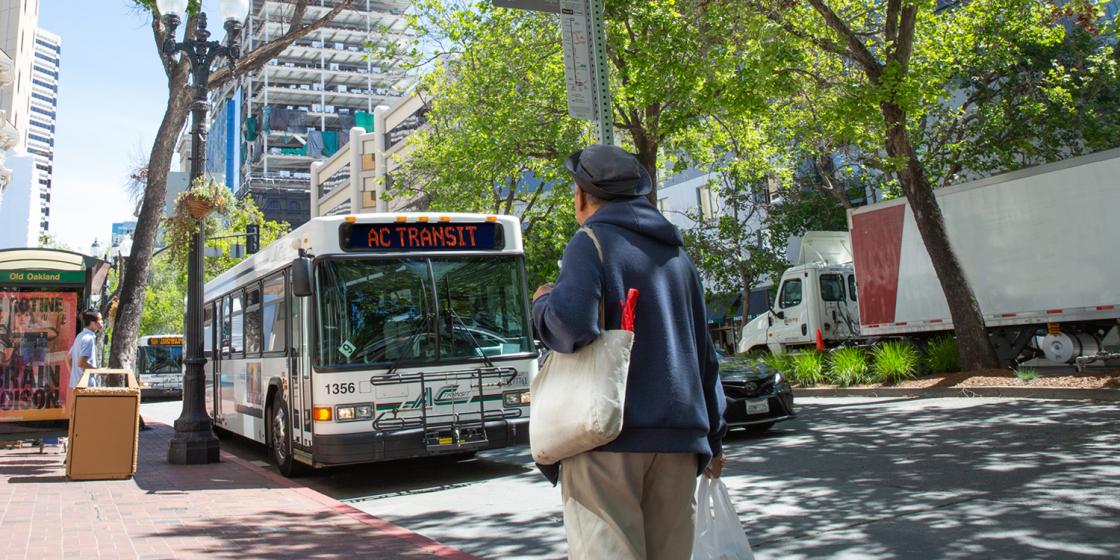 AC Transit bus driving on street; pedestrian looking on