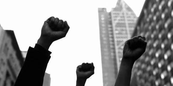 A black and white photo showing three hands raised in a fist to the sky.