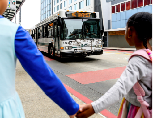 two children hold hands in front of a bus